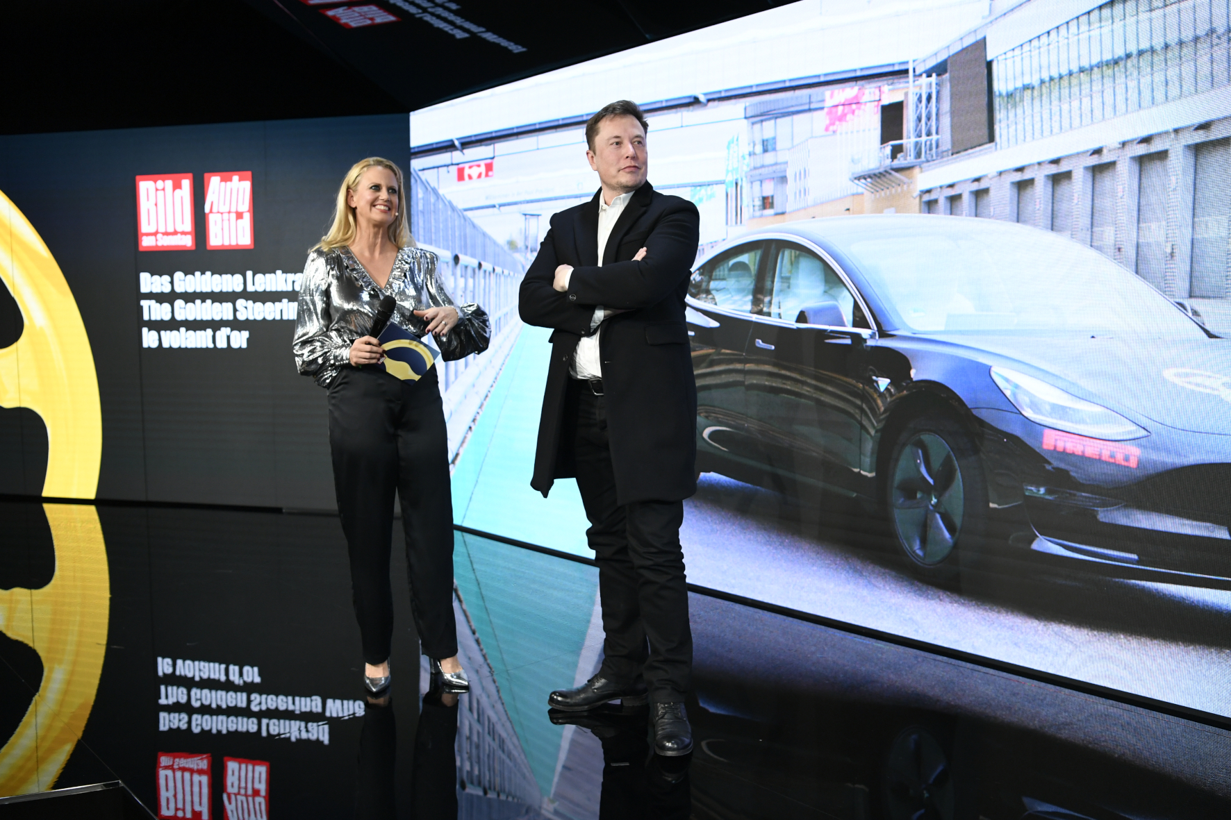 mid Groß-Gerau - Hoher Besuch: Moderatorin Barbara Schöneberger mit Tesla-Boss Elon Musk vor einem Bild des ausgezeichneten Model 3. Axel Springer / Niels Starnick